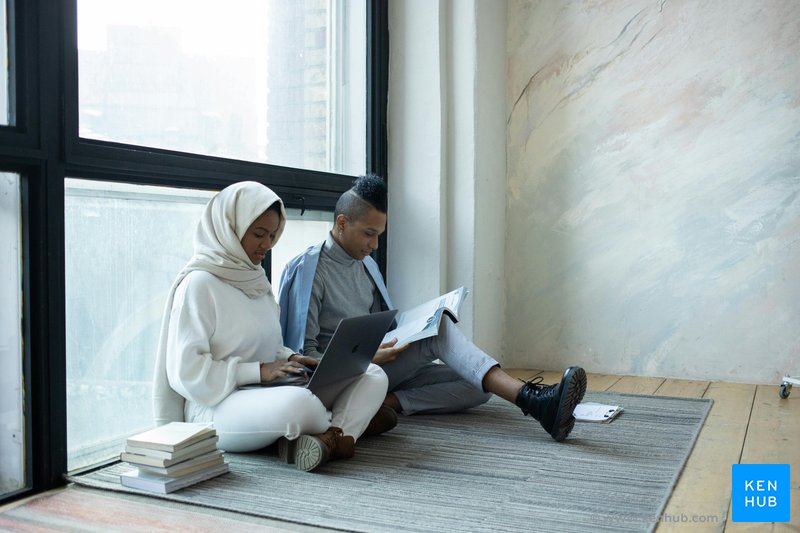 An image of two students sitting next to a window while studying